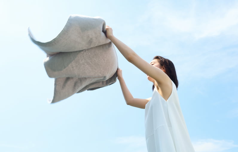 乾きやすいmunioのタオルを青空の下で広げる女性